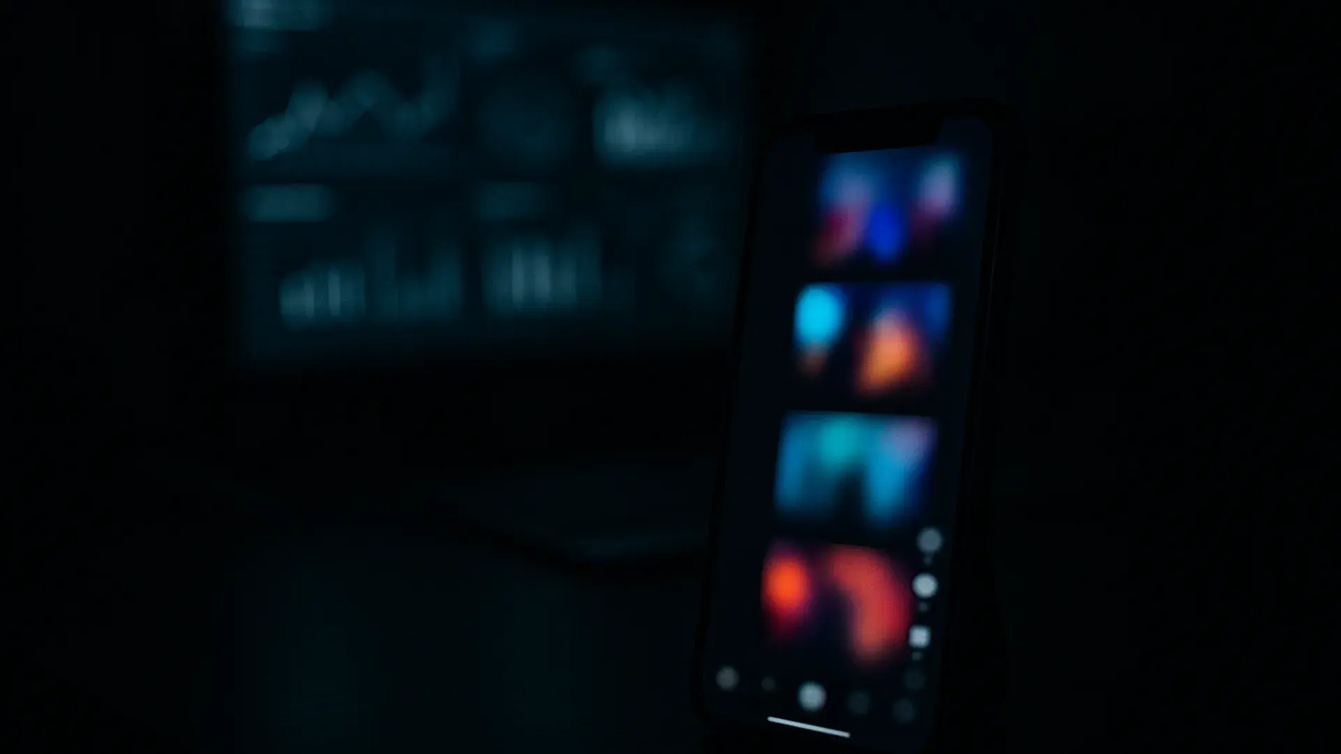 Vertical short-form video feed on a phone in a dark editing workspace, analytics glowing behind
